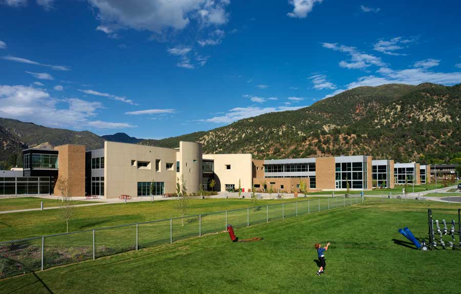 High school building and a child playing in the foreground and mountains in the background