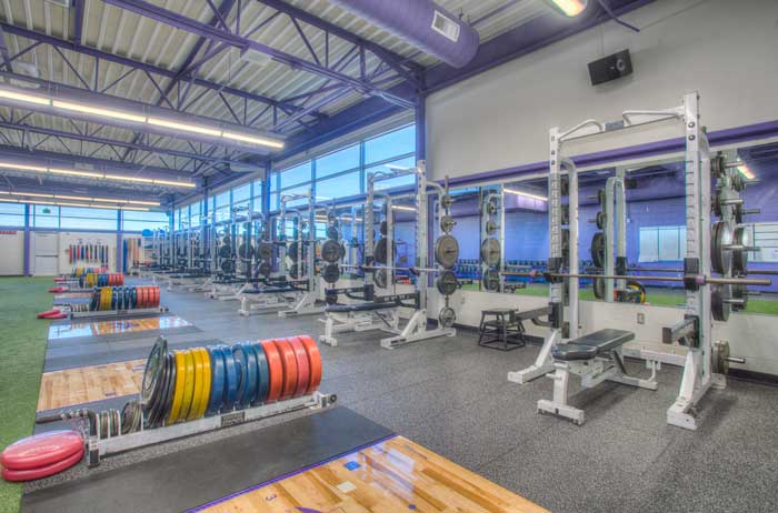 Interior view of Littleton High School's gymnasium, featuring a spacious layout with high ceilings, wooden bleachers, and a central basketball court. The design highlights the athletic focus of the school, with bright lighting and open seating areas.