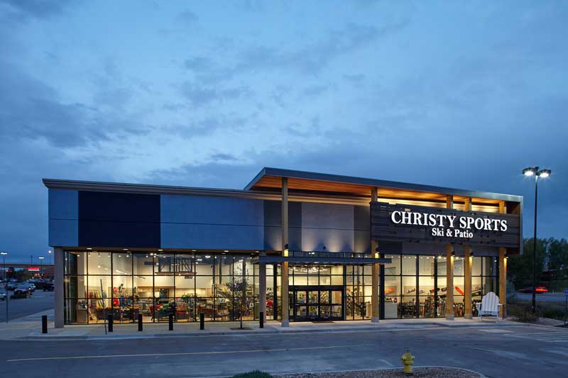 Exterior of the Christy Sports building at night with cloudy skies and a fully lit interior. 