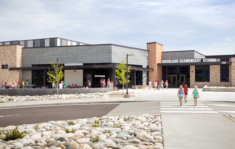 Exterior view of Douglas Elementary School's main entrance walkway, showcasing a modern design with a mix of brick and metal materials. The entrance is framed by large windows and a covered walkway, creating a welcoming and functional entry point for students and visitors.