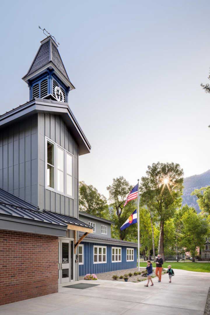 Exterior view of Lake City School, featuring a modern design with a combination of wood, stone, and metal materials. The building is set against a mountainous backdrop, with large windows and a welcoming entrance enhancing its connection to the natural surroundings.