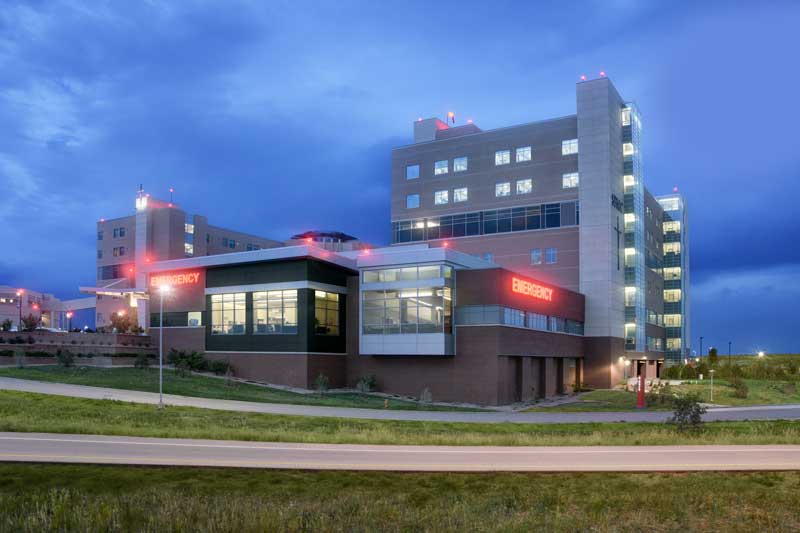 Exterior view of the SFMC IMCU/CCU expansion, featuring a modern hospital design with large windows, a combination of brick and metal materials, and a well-landscaped surrounding. The structure integrates seamlessly with the existing medical campus, emphasizing functionality and patient care.