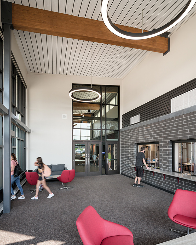 entry vestibule in a middle school; two students are walking out of the doors and one student is standing in front of the window to the administration area