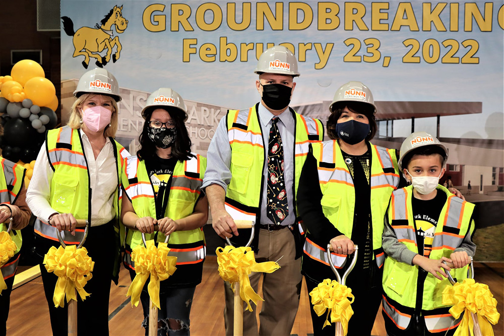 a group in hard hats and vests standing with shovels celebrating the ground breaking