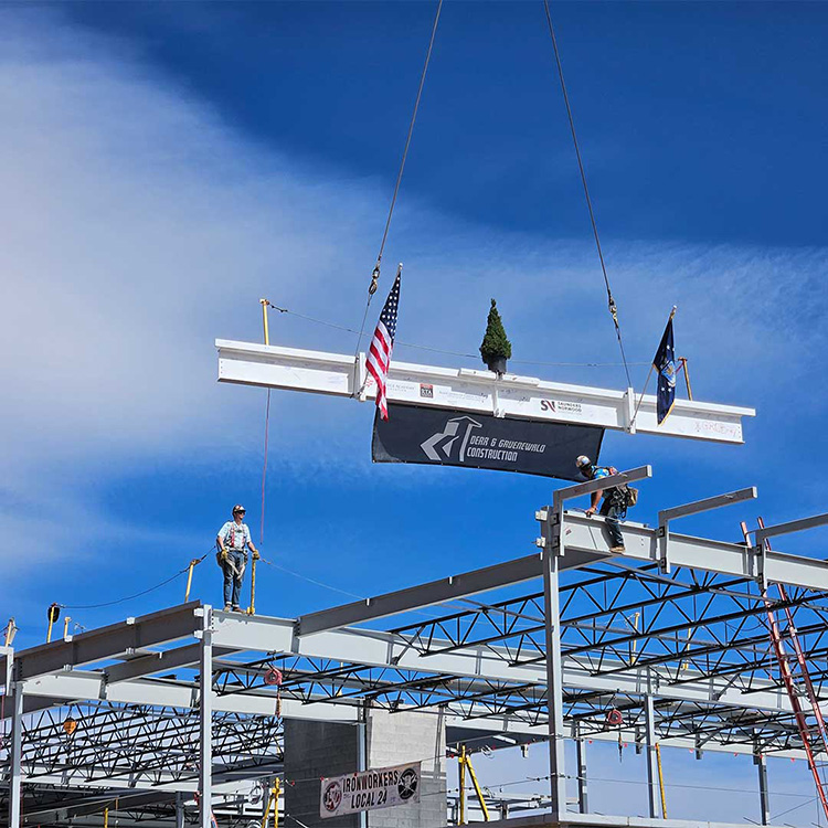 Crane cables lowering steel beams toward construction workers